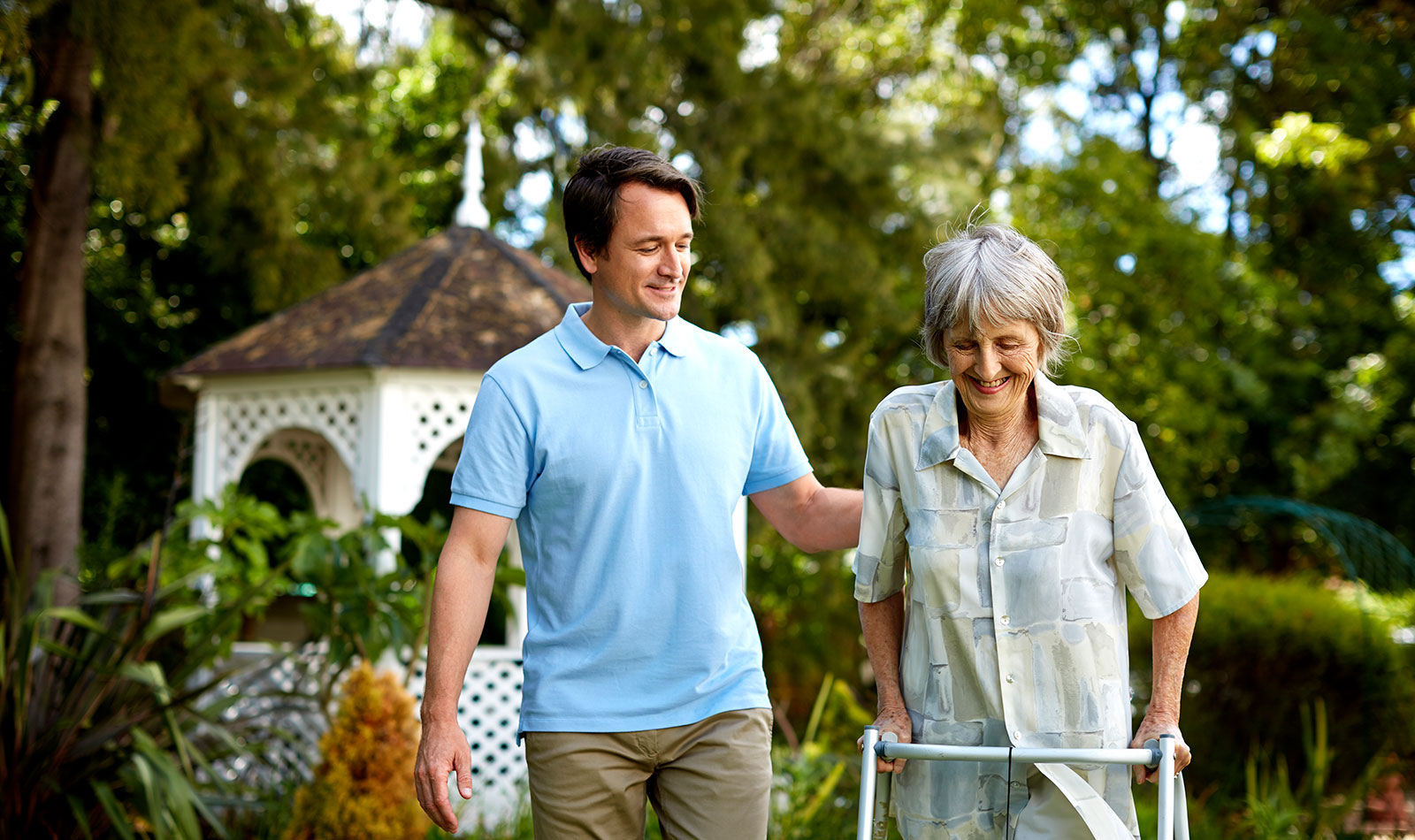 male caregiver walking with senior woman who is using an assistive walking device
